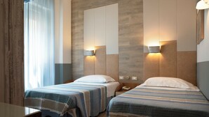 Ein Hotelzimmer mit zwei Betten, jeweils mit einer gestreiften Tagesdecke, einem Holzkopfstück und Wandleuchten zum Lesen.
