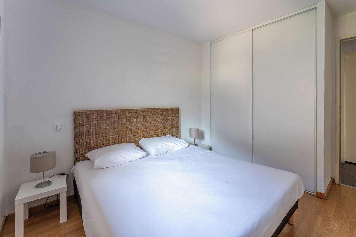 Una cama bien hecha en una habitación con cabecera blanca, una mesita de noche pequeña con lámpara y una puerta corredera.
