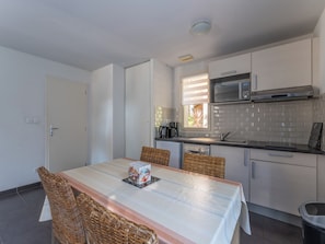 A compact kitchen with a dining table, wicker chairs, a microwave, and a dishwasher. - Residence Les Rives du Lac - Vacancéole (Lacanau)