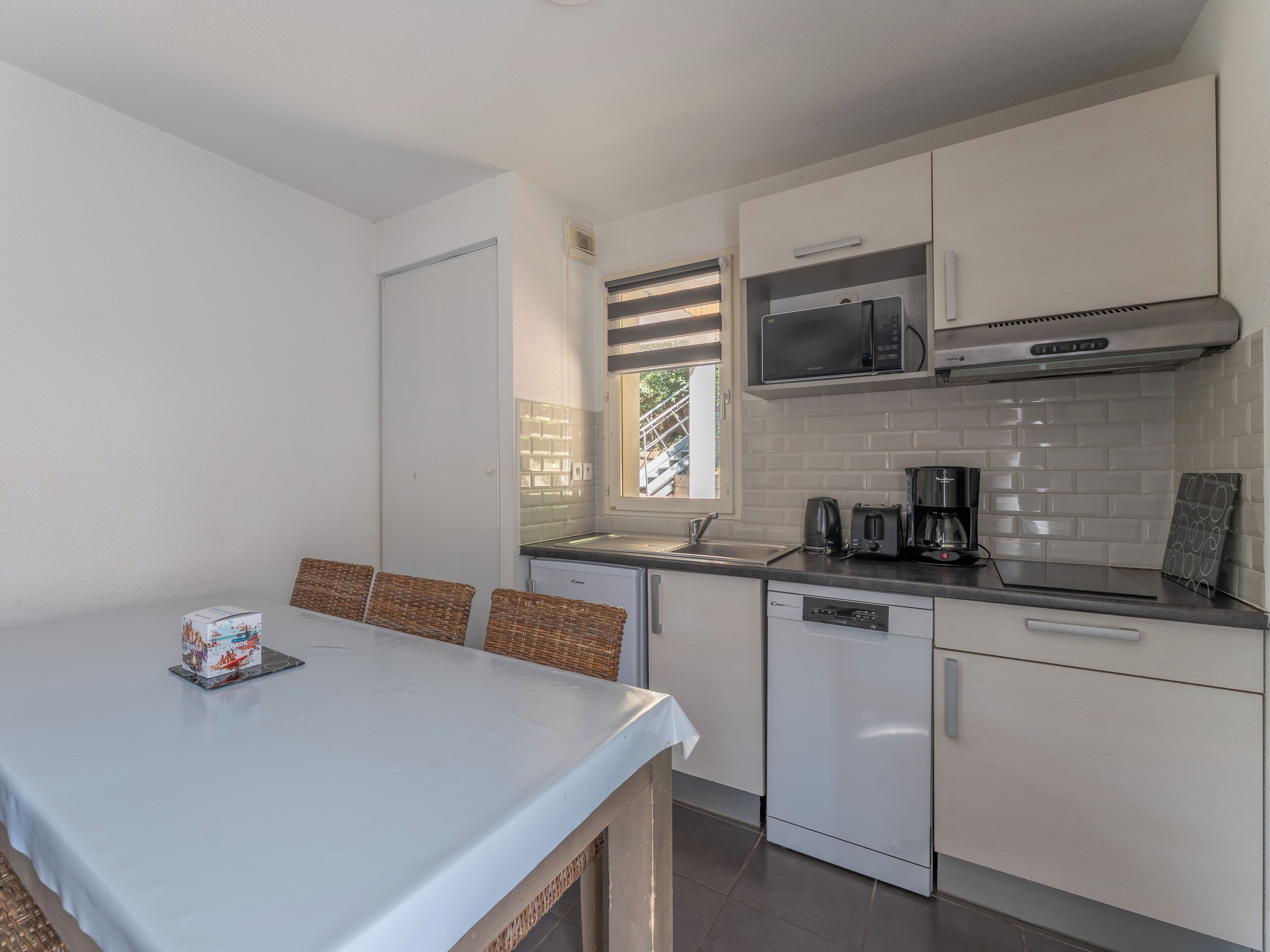A compact kitchen with white cabinets, a microwave, a coffee maker, and a dishwasher.