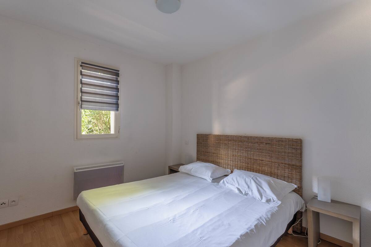 Un dormitorio con cama, mesita de noche, radiador y ventana con persianas.
