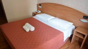 A neatly made bed with white linens, a red bedspread, and two rolled towels on the bed. - Hotel Nuovo (Milan)