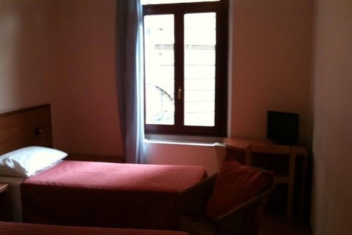 Une chambre avec deux lits, une chaise, une petite table et une fenêtre.