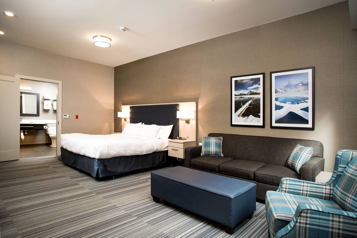 A hotel room with a bed, a sofa, a coffee table, and two framed pictures on the wall.