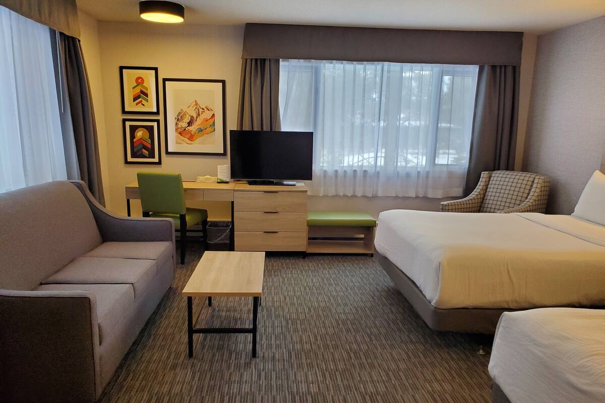 A hotel room with a bed, a sofa, a desk with a television, and a window with curtains.