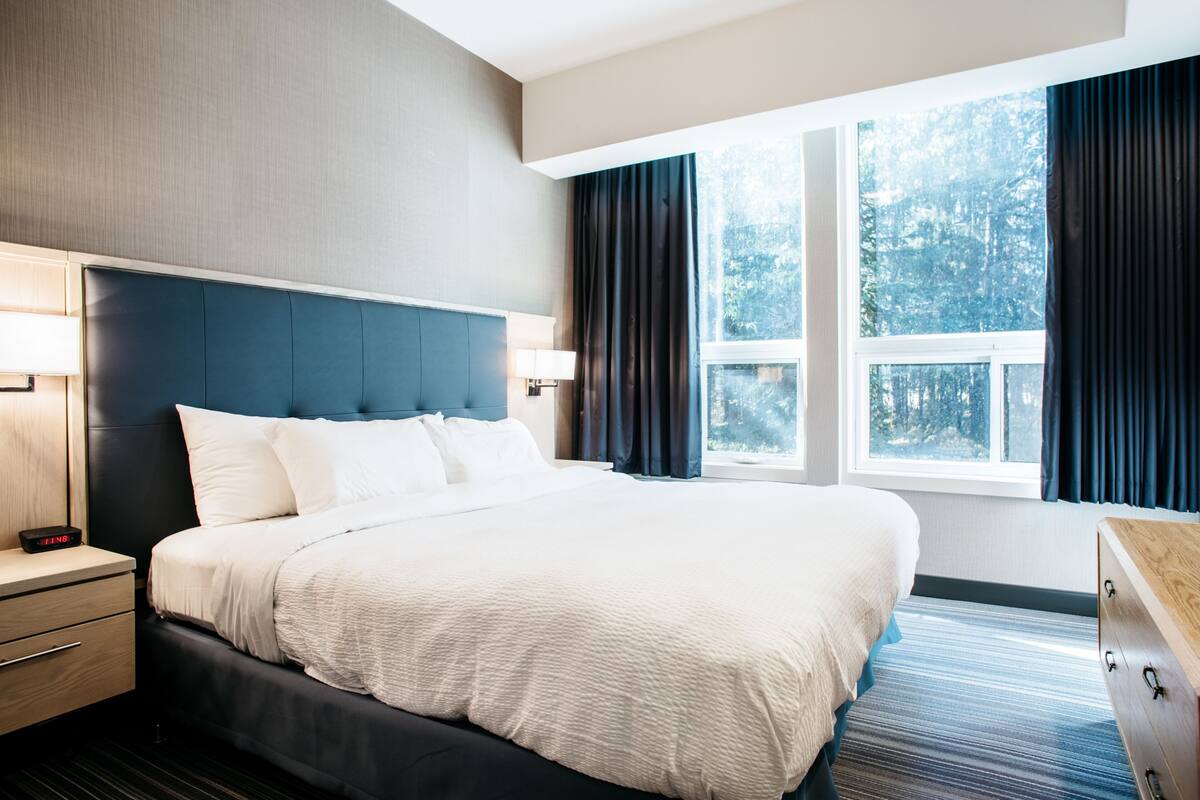 A hotel room with a large bed, a nightstand, a dresser, and a window with curtains.