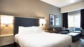 A modern hotel room with a large bed, bedside tables, a sofa, a chair, and a window with curtains.