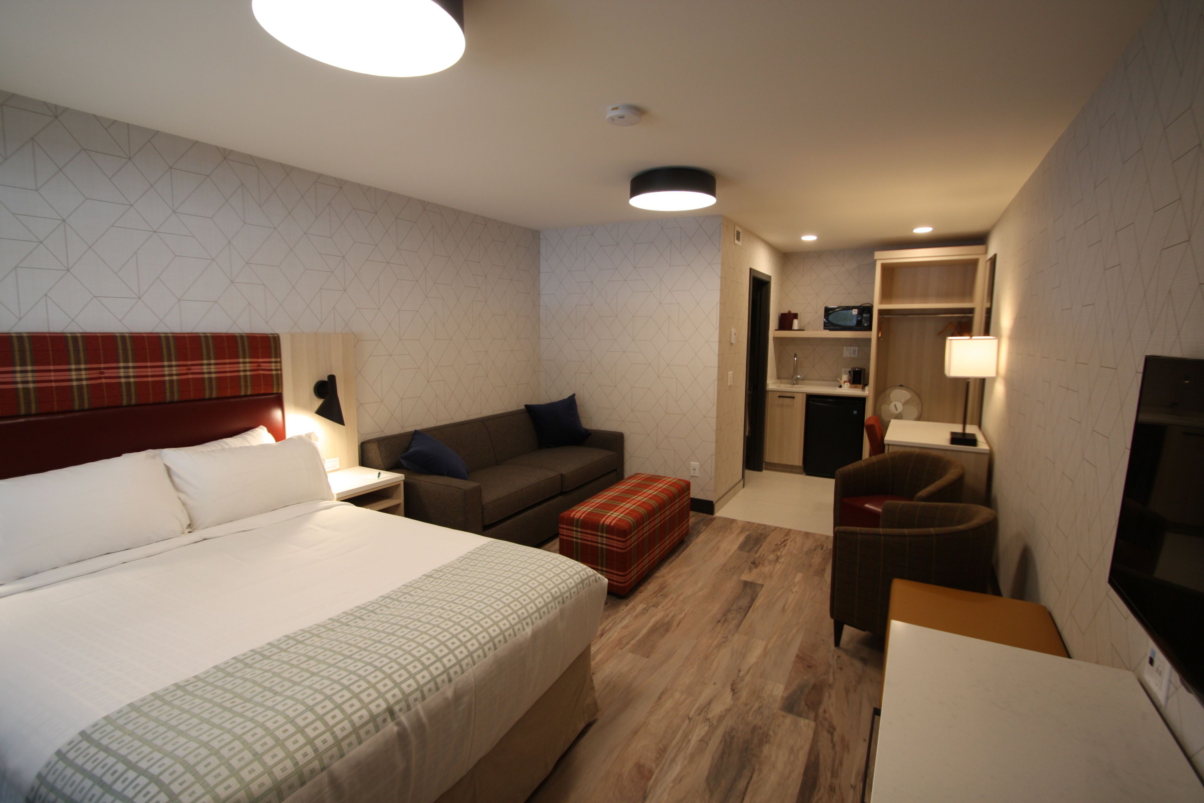 Una habitación de hotel con una cama grande, un sofá, una mesita, una silla y un televisor.