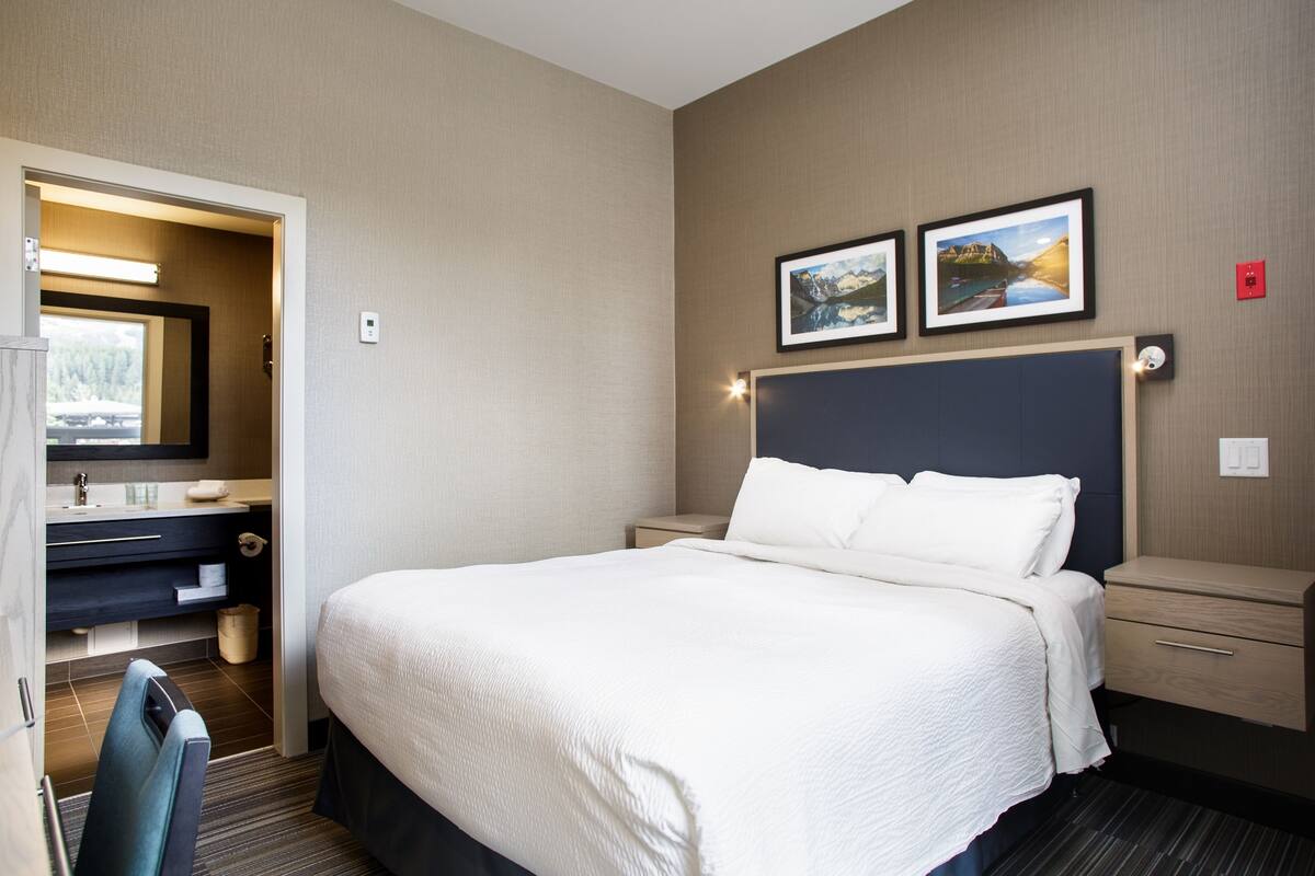 A hotel room with a large bed, a desk with a chair, a vanity with a mirror, and two framed pictures on the wall.