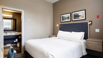 Quarto de hotel com uma cama grande, uma mesa com cadeira, uma cômoda com espelho e duas fotos emolduradas na parede.