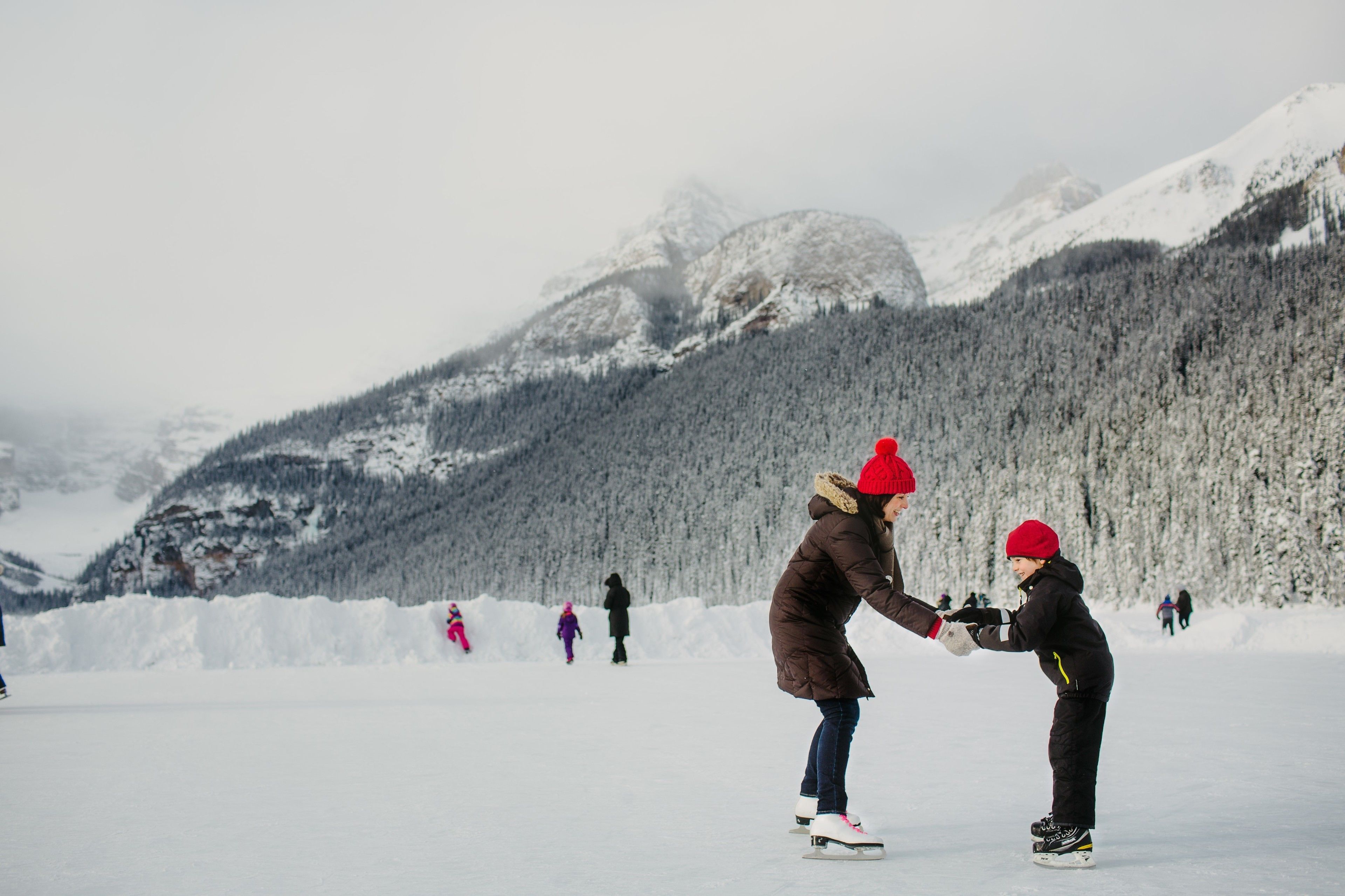 Un paisaje nevado con una persona enseñando a un niño a patinar sobre hielo.