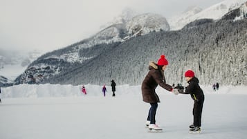 Un paisaje nevado con una persona enseñando a un niño a patinar sobre hielo.