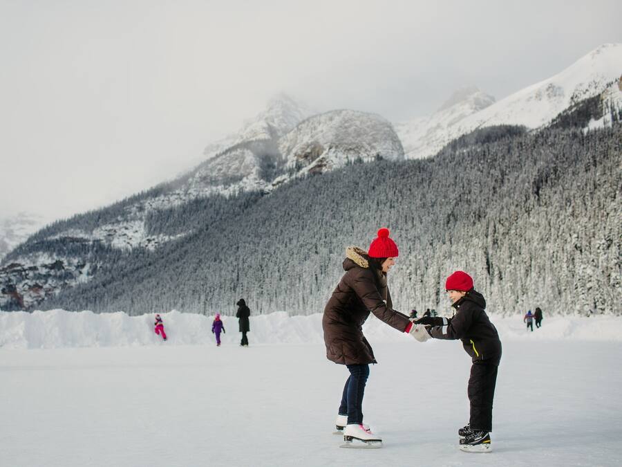 Un paisaje nevado con una persona enseñando a un niño a patinar sobre hielo.