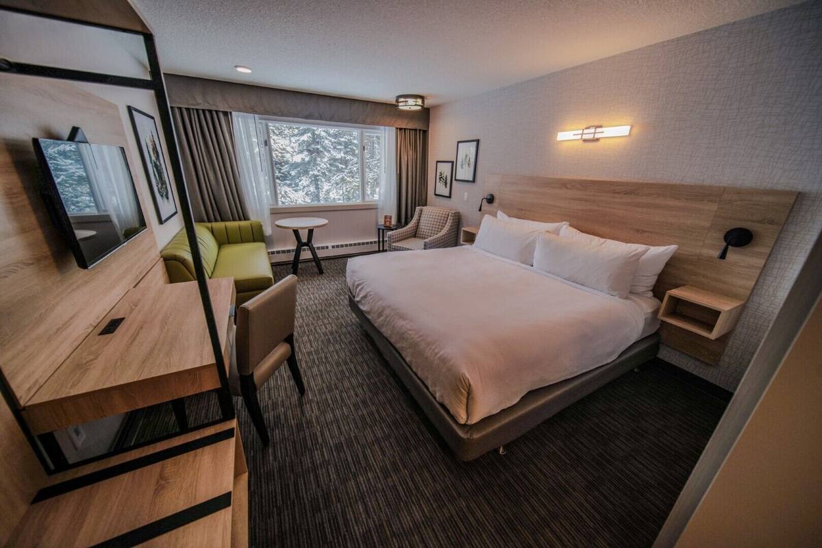 A modern hotel room with a large bed, a desk, a chair, a small table, and a TV.