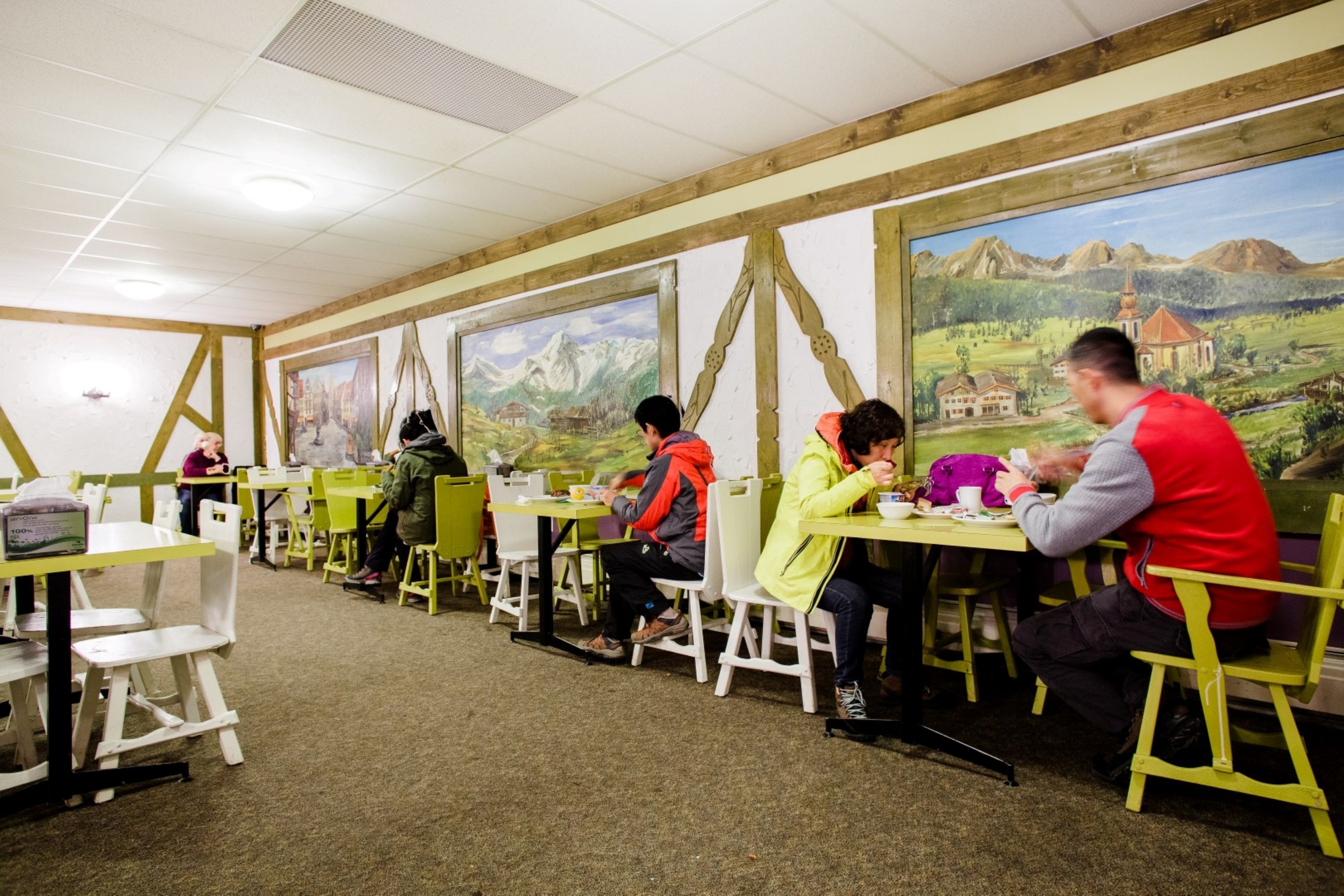 A dining area with tables and chairs, a mural on the wall, and a ceiling with recessed lighting.