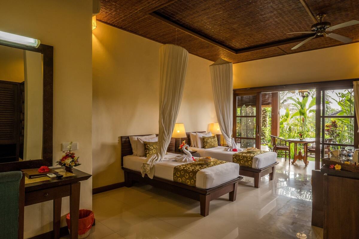 A hotel room with two beds, a sitting area, and a view of the outdoors.