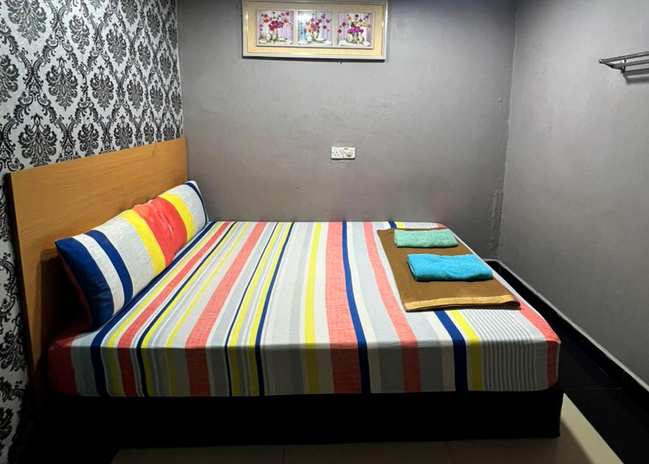 A bedroom with a striped bedspread, a wooden headboard, and a framed floral artwork on the wall.