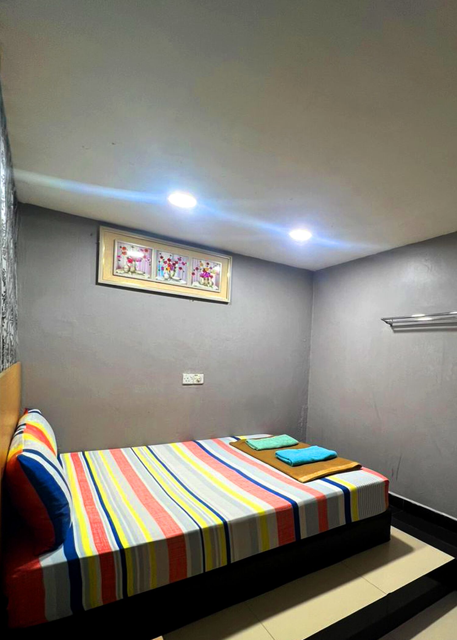 A small, private room with a single bed, a framed picture on the wall, and a small table with a towel.