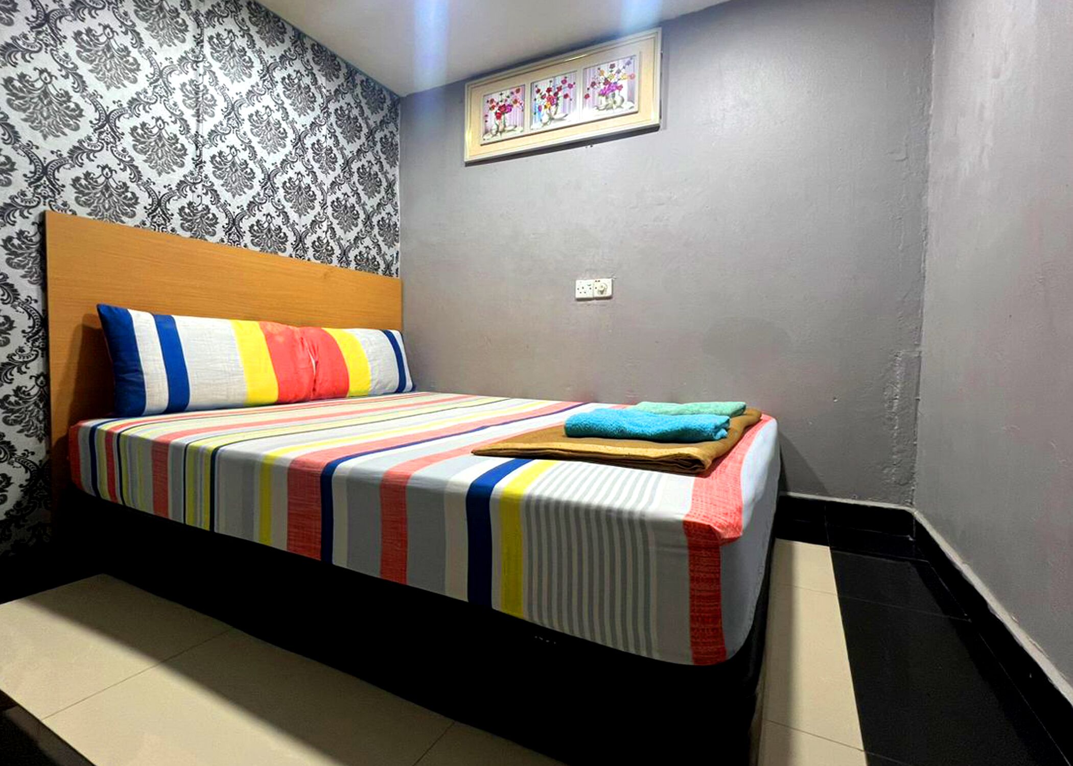 A bedroom with a bed, patterned wallpaper, a framed picture, and a tiled floor.