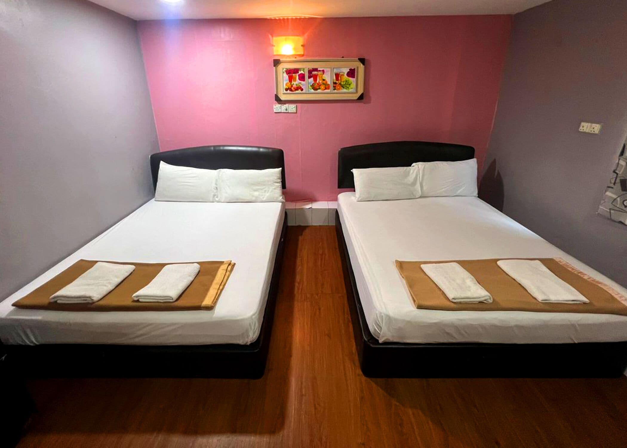Une chambre d’hôtel avec deux lits simples, chacun doté d’une tête de lit en bois, de draps blancs et d’une serviette marron posée sur le lit.