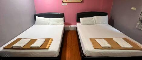 Une chambre d’hôtel avec deux lits simples, chacun doté d’une tête de lit en bois, de draps blancs et d’une serviette marron posée sur le lit.