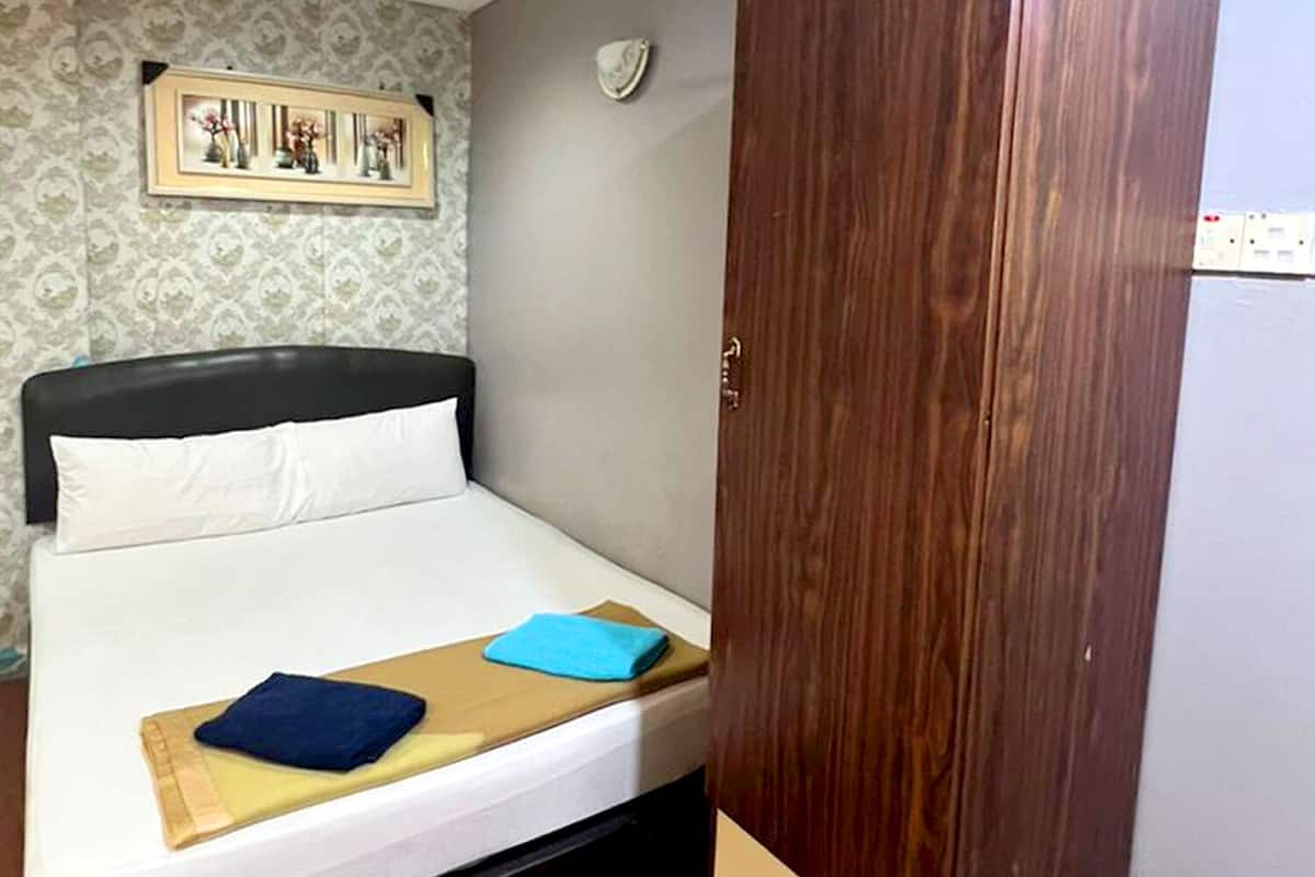 A bedroom with a bed, a wooden wardrobe, a framed picture on the wall, and a ceiling light.