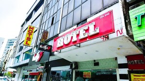 Um hotel com uma placa vermelha grande, várias placas menores e uma entrada visível.