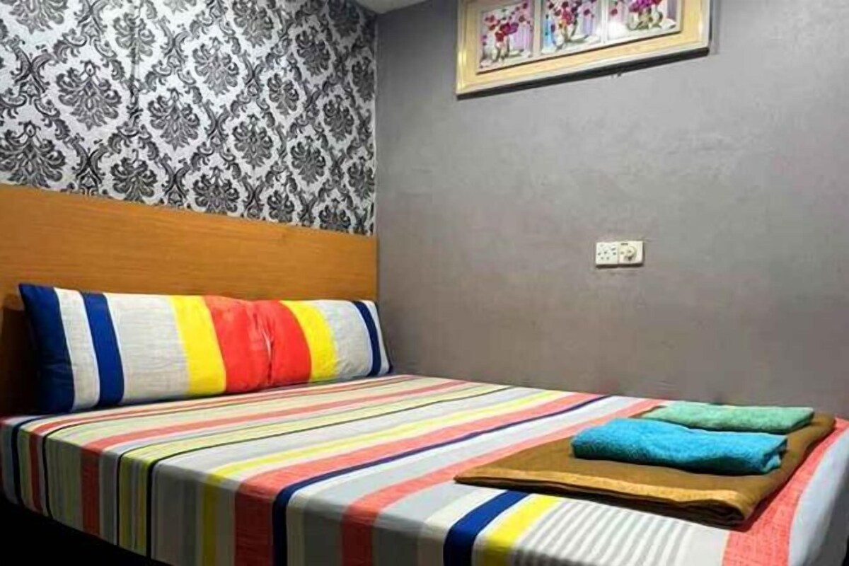 A single bed with a striped bedspread and pillows, a wooden headboard, a patterned wallpaper, and a framed picture on the wall.