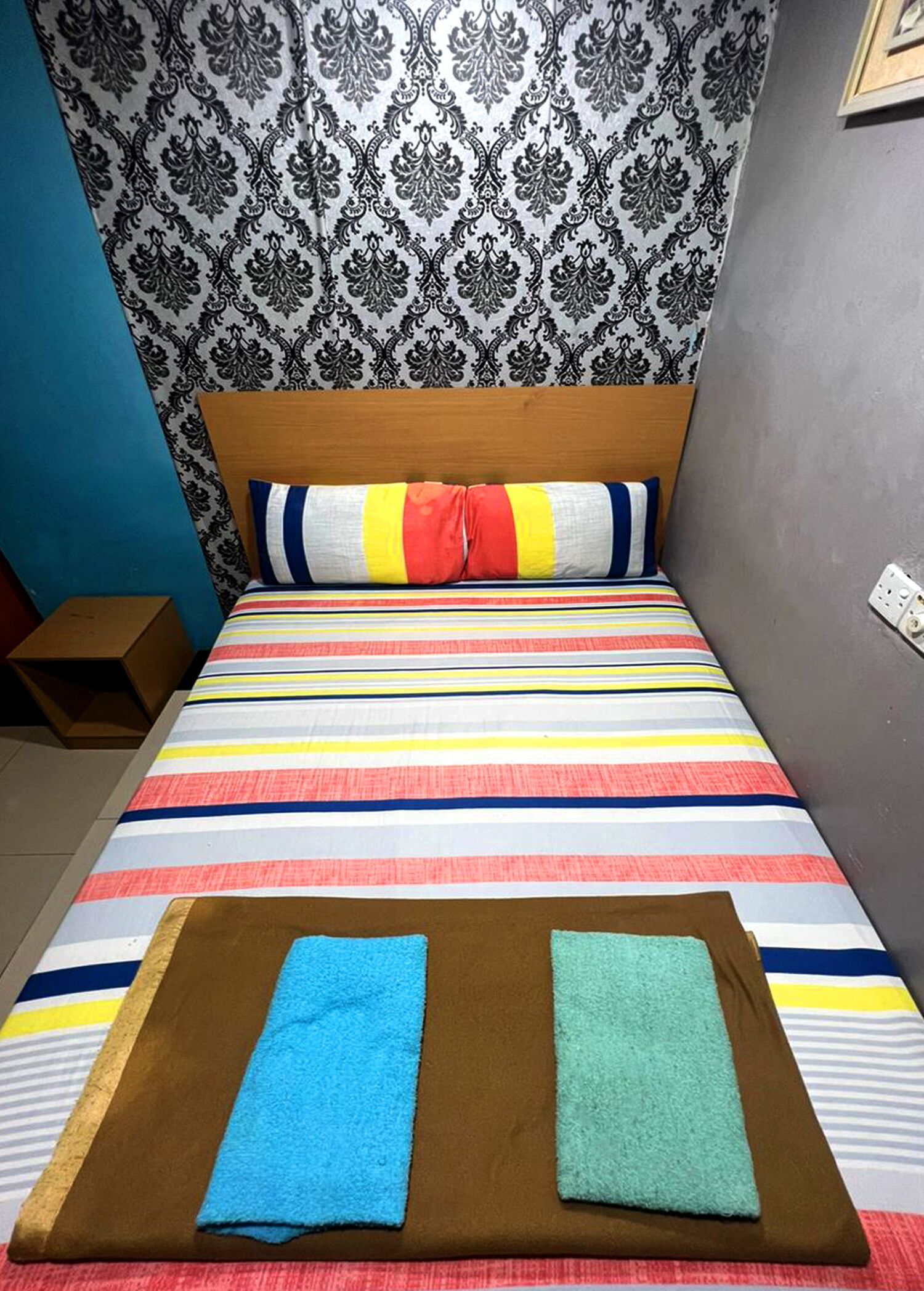 Una cama con colcha a rayas, almohadas y dos toallas dobladas sobre un corredor de cama marrón.