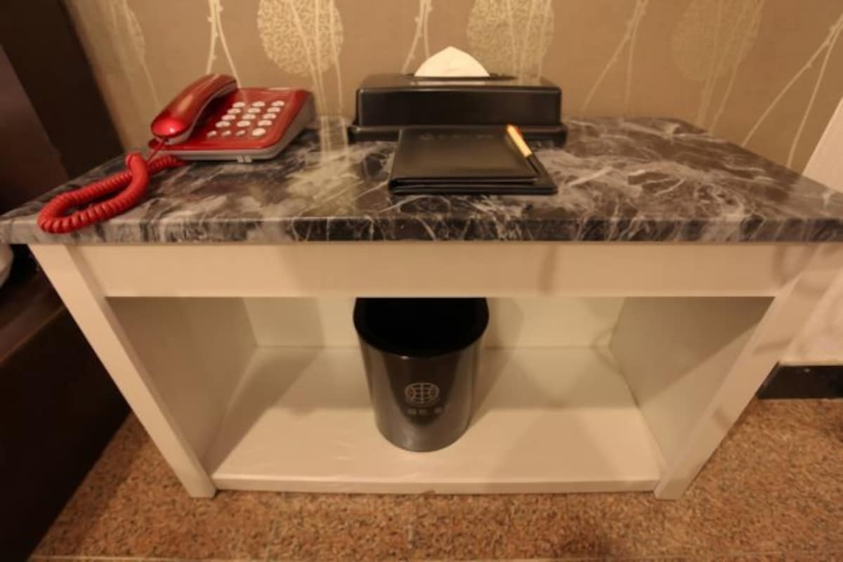 Uma bancada de mármore com um telefone vermelho, uma caixa de lenços de papel pretos e uma carteira preta.