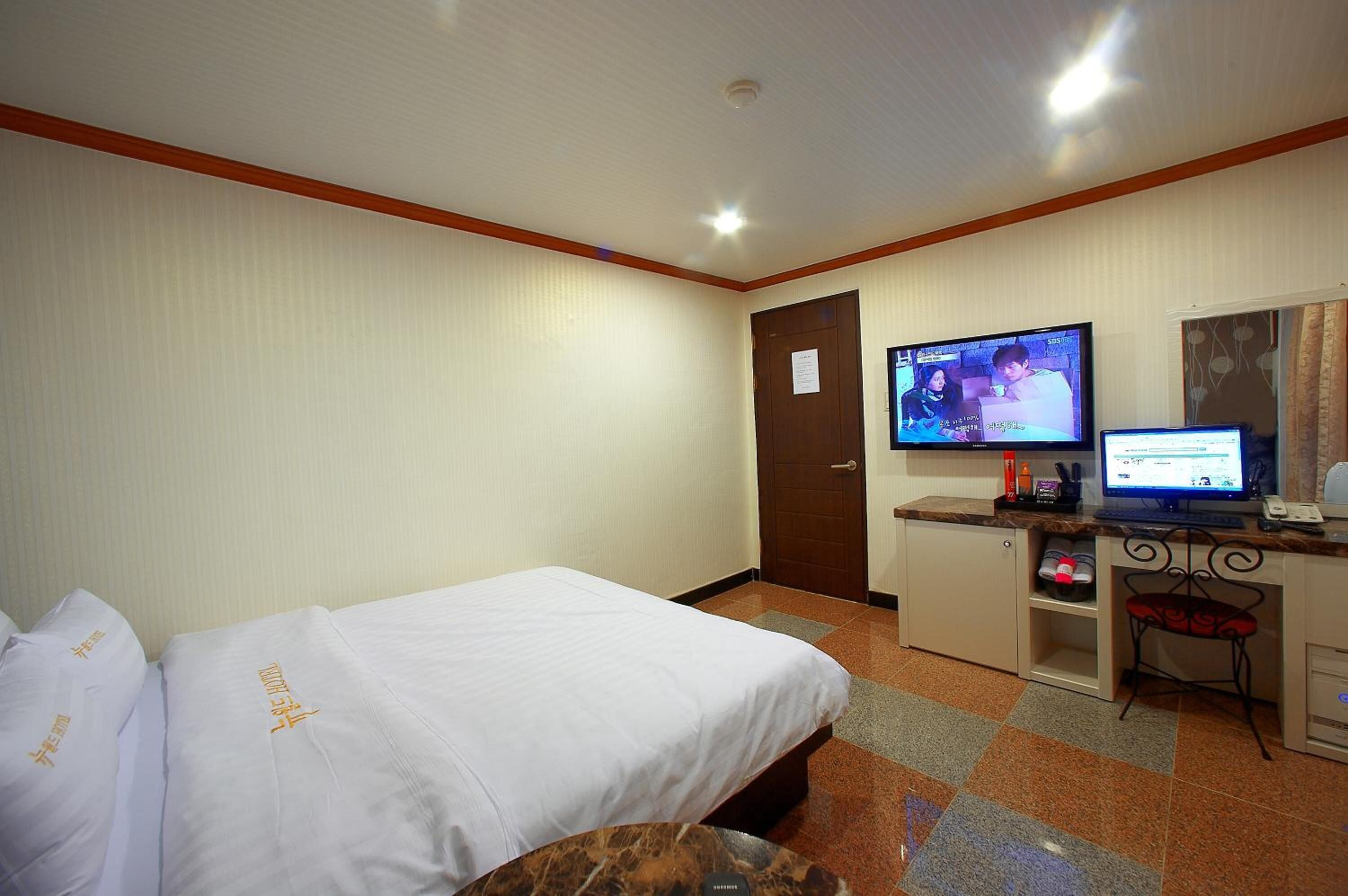 A hotel room with two beds, a desk with a computer, a television, and a small seating area.