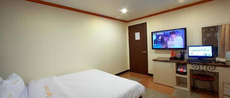 A hotel room with two beds, a desk with a computer, a television, and a small seating area.