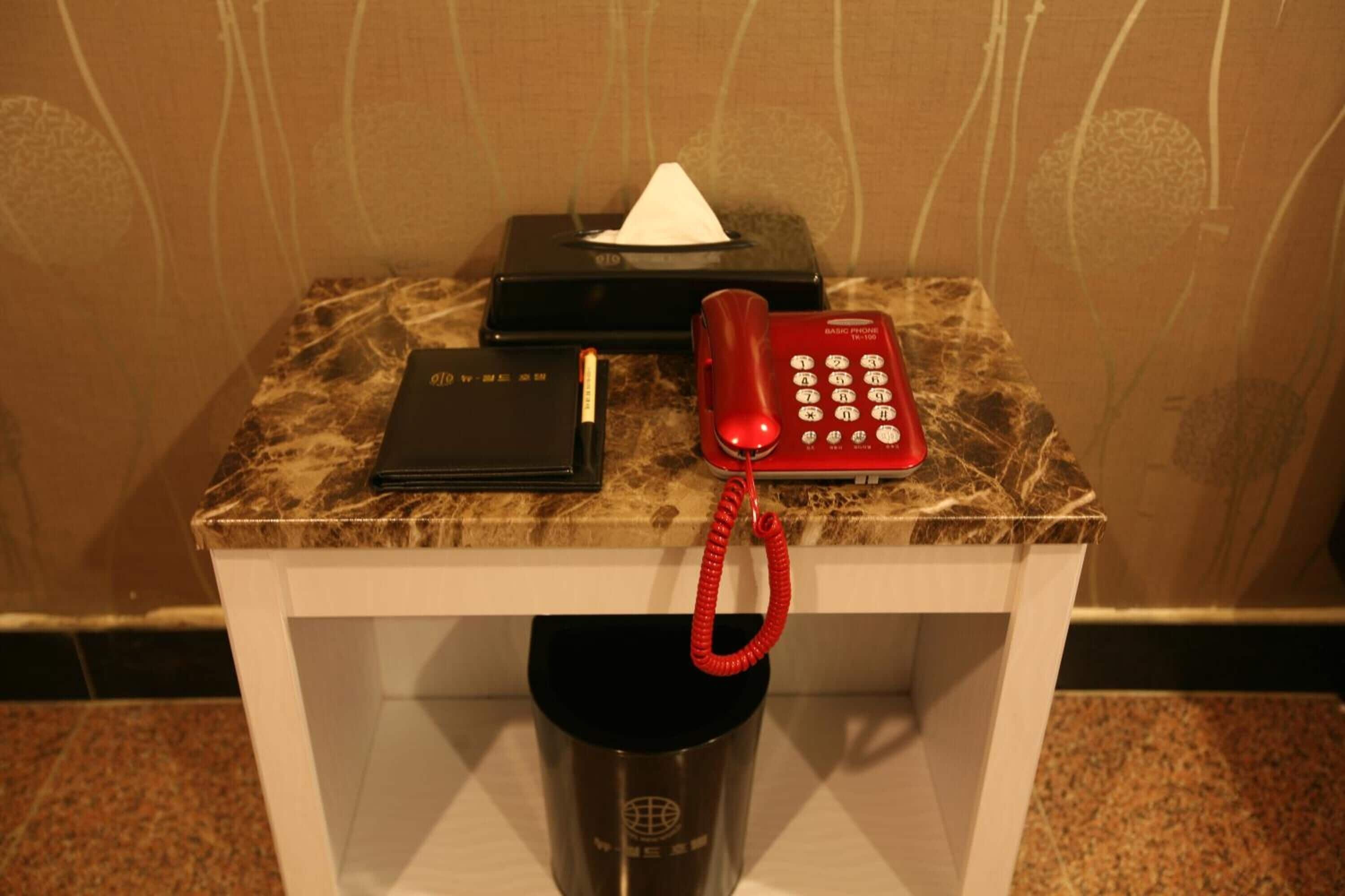 A marble-topped table with a red telephone, a black box, a tissue, and a black tumbler.