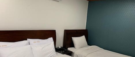 Habitación de hotel con dos camas, cada una con ropa blanca de cama y almohadas, cabeceros de madera y un equipo de aire acondicionado montado en la pared.