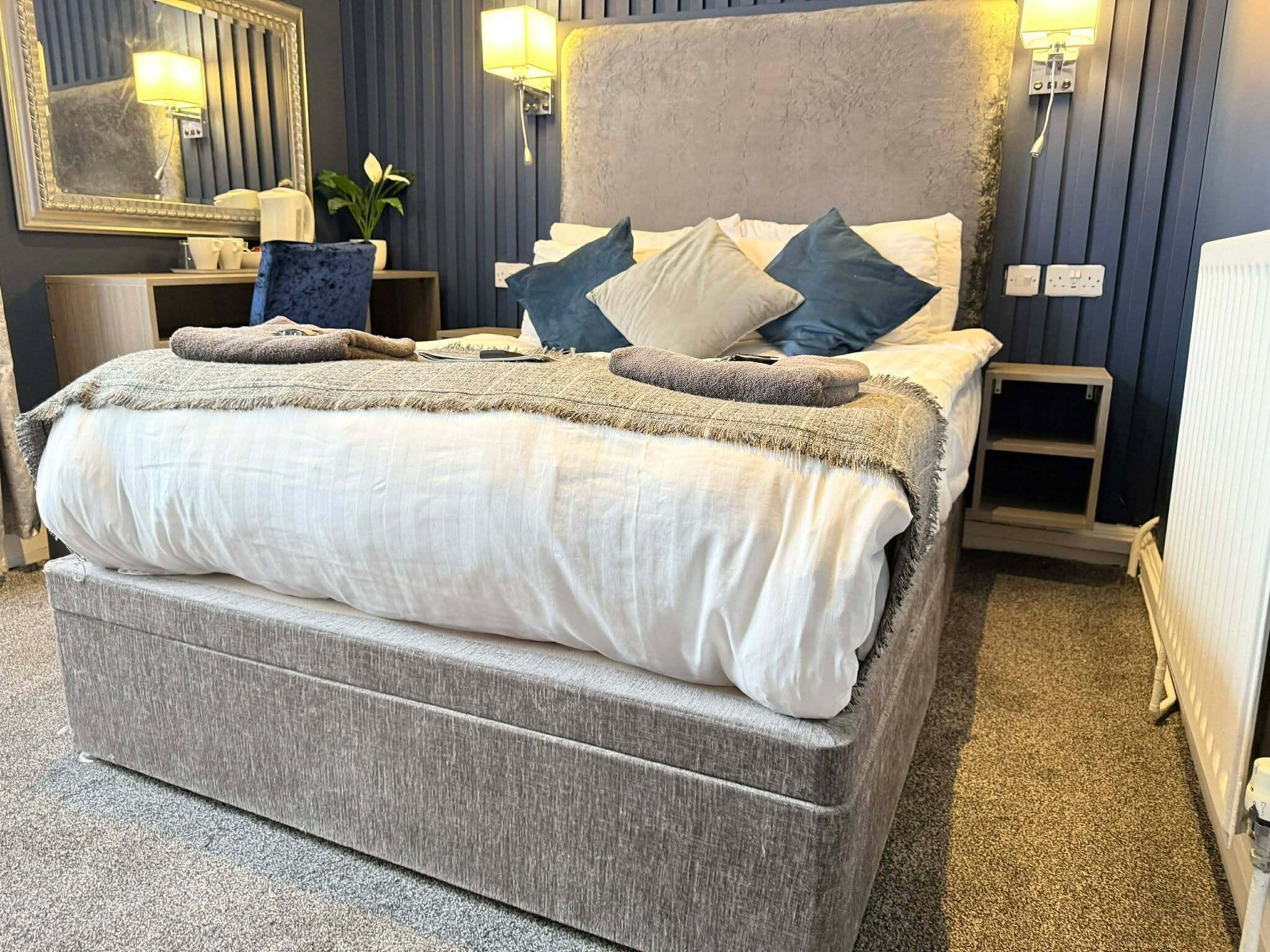 Une chambre à coucher avec un grand lit, une table de chevet, un miroir et une lampe fixée au mur.