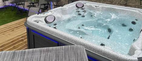 A hot tub with a stone exterior, surrounded by a wooden deck and outdoor furniture.