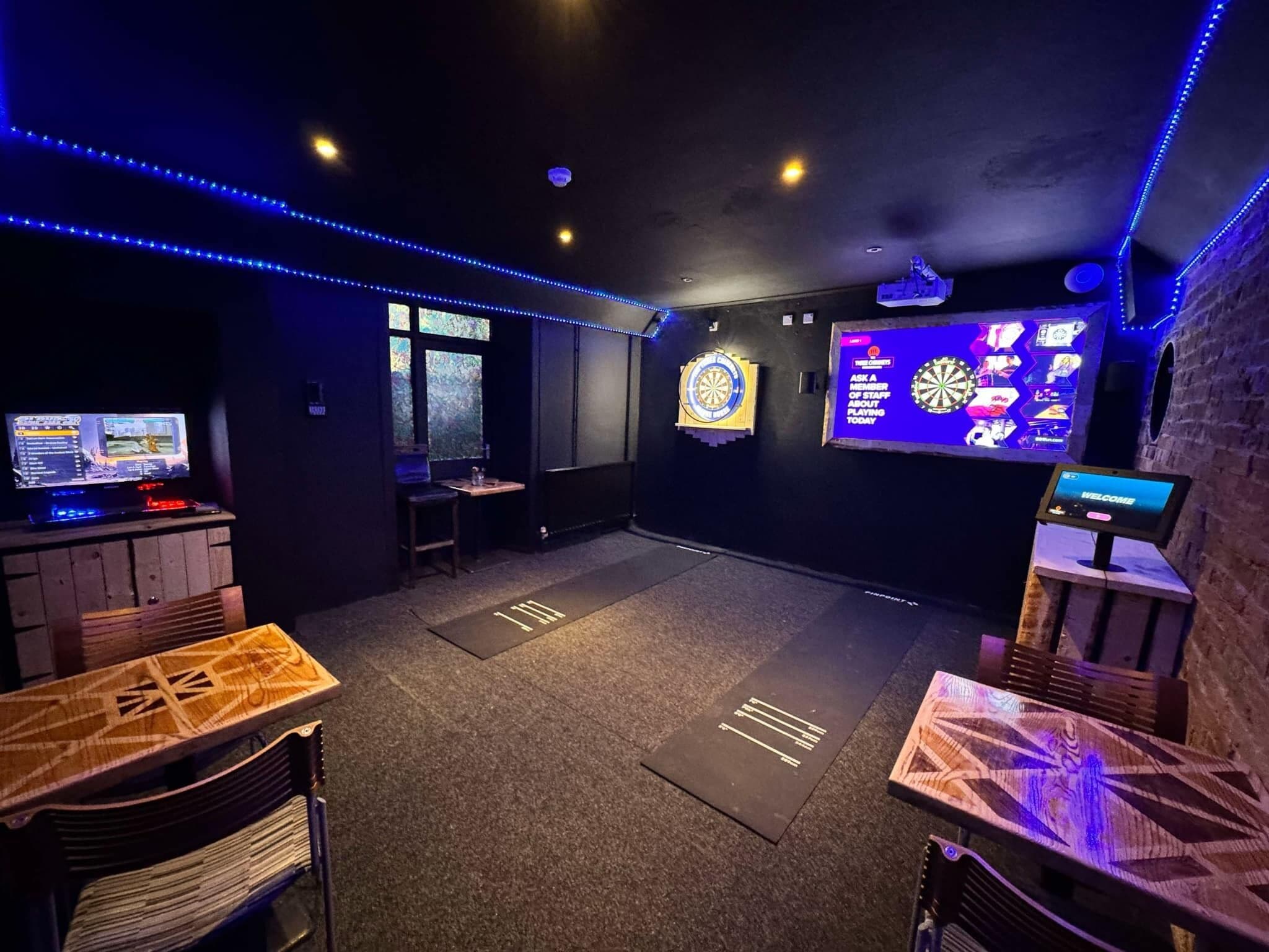A room with a dartboard, a TV screen, and a dartboard with a sign.