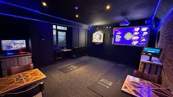 A room with a dartboard, a TV screen, and a dartboard with a sign.