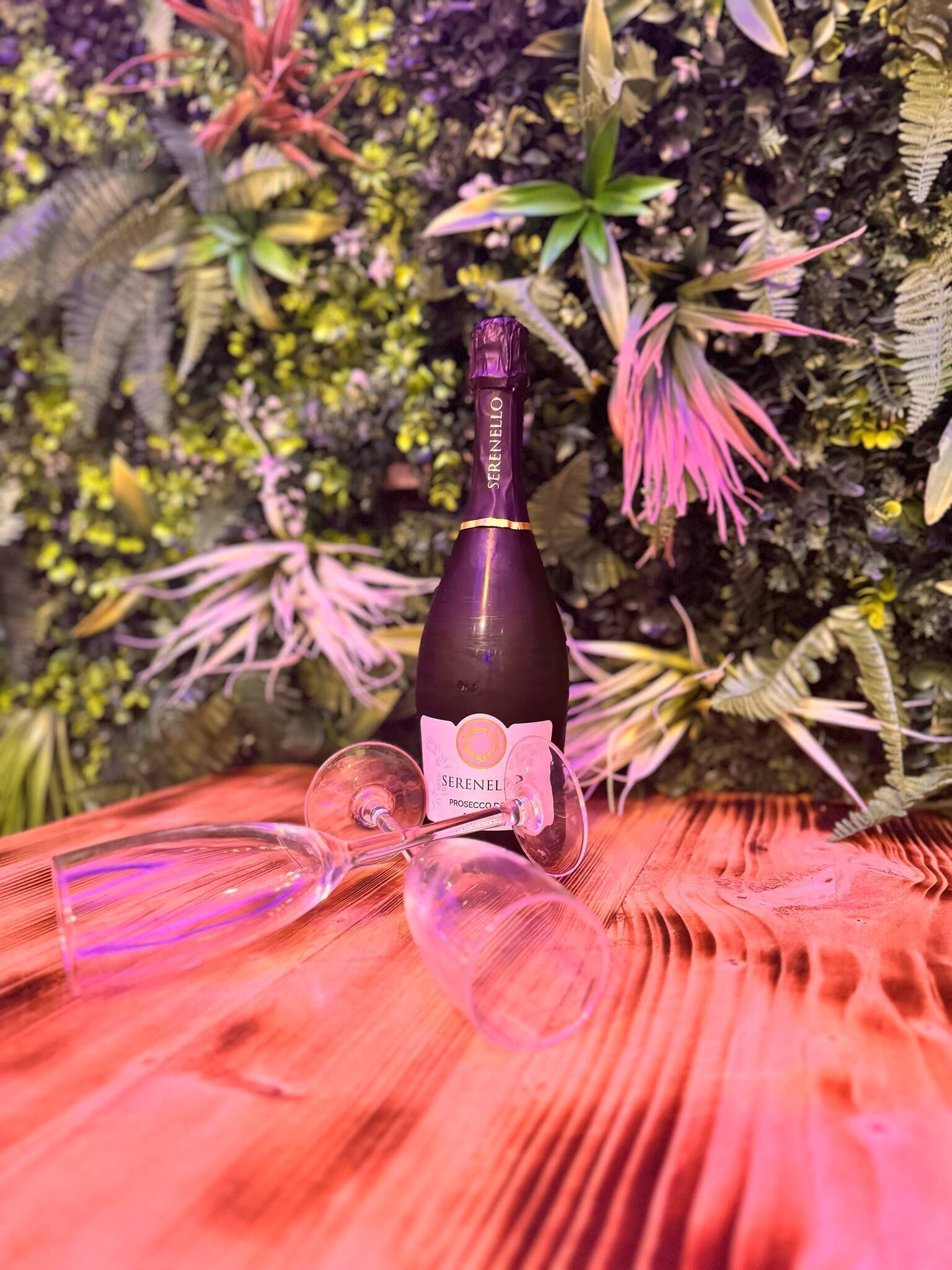 A bottle of Serenello Prosecco on a wooden surface with a blurred background of foliage.