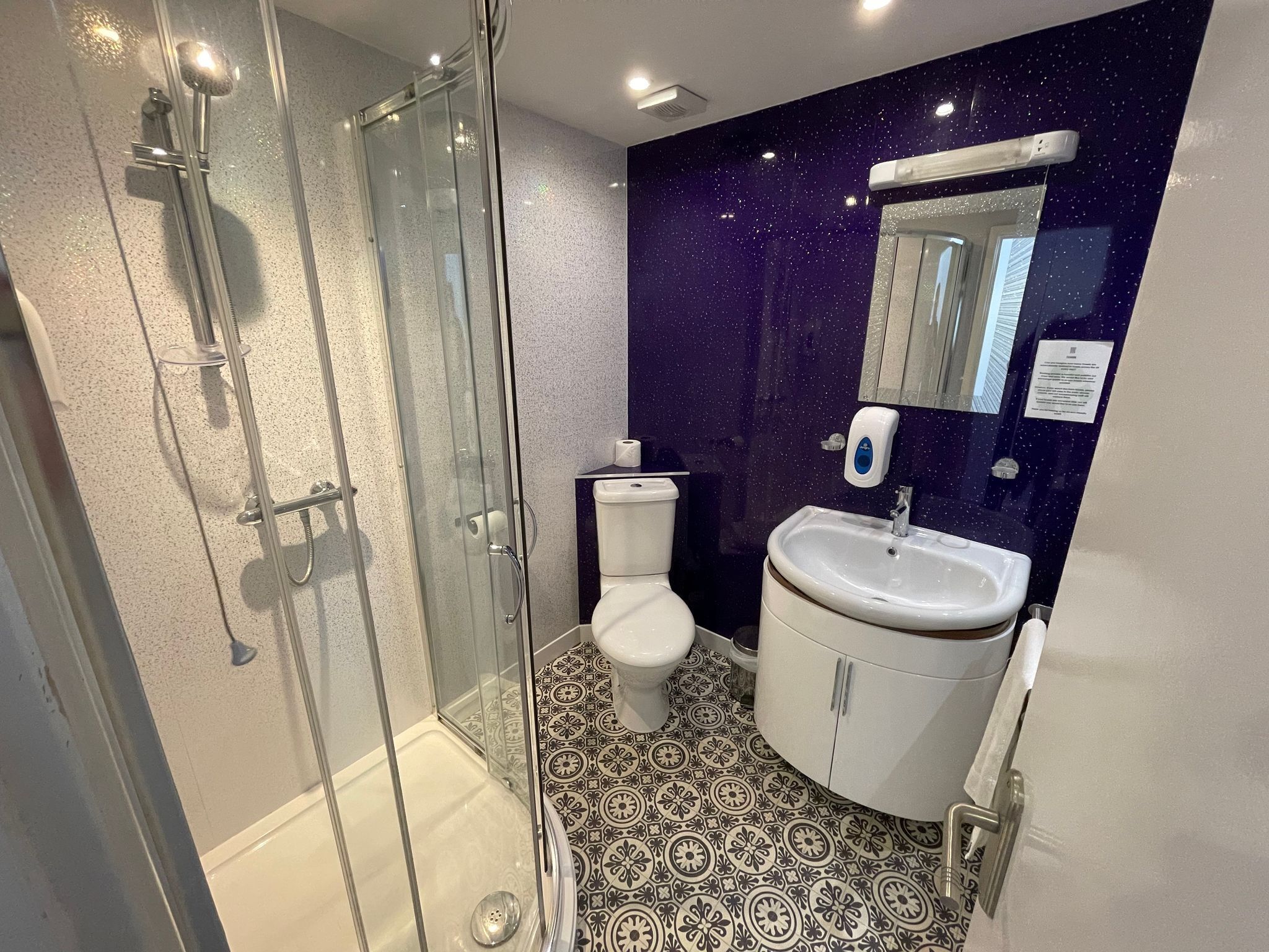A bathroom with a glass-enclosed shower, a toilet, a sink, and a mirror.