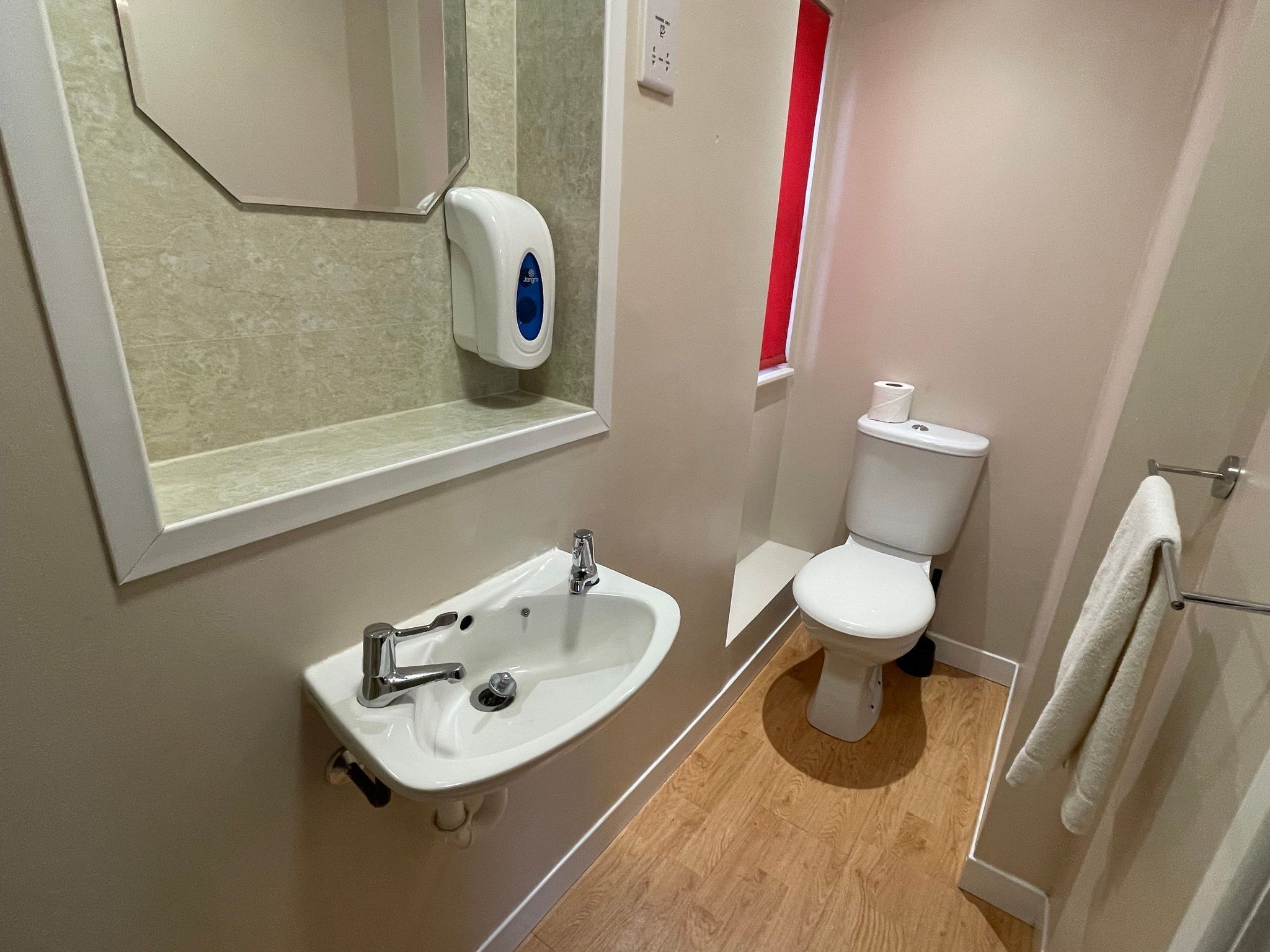 A bathroom with a sink, toilet, and a hand soap dispenser.
