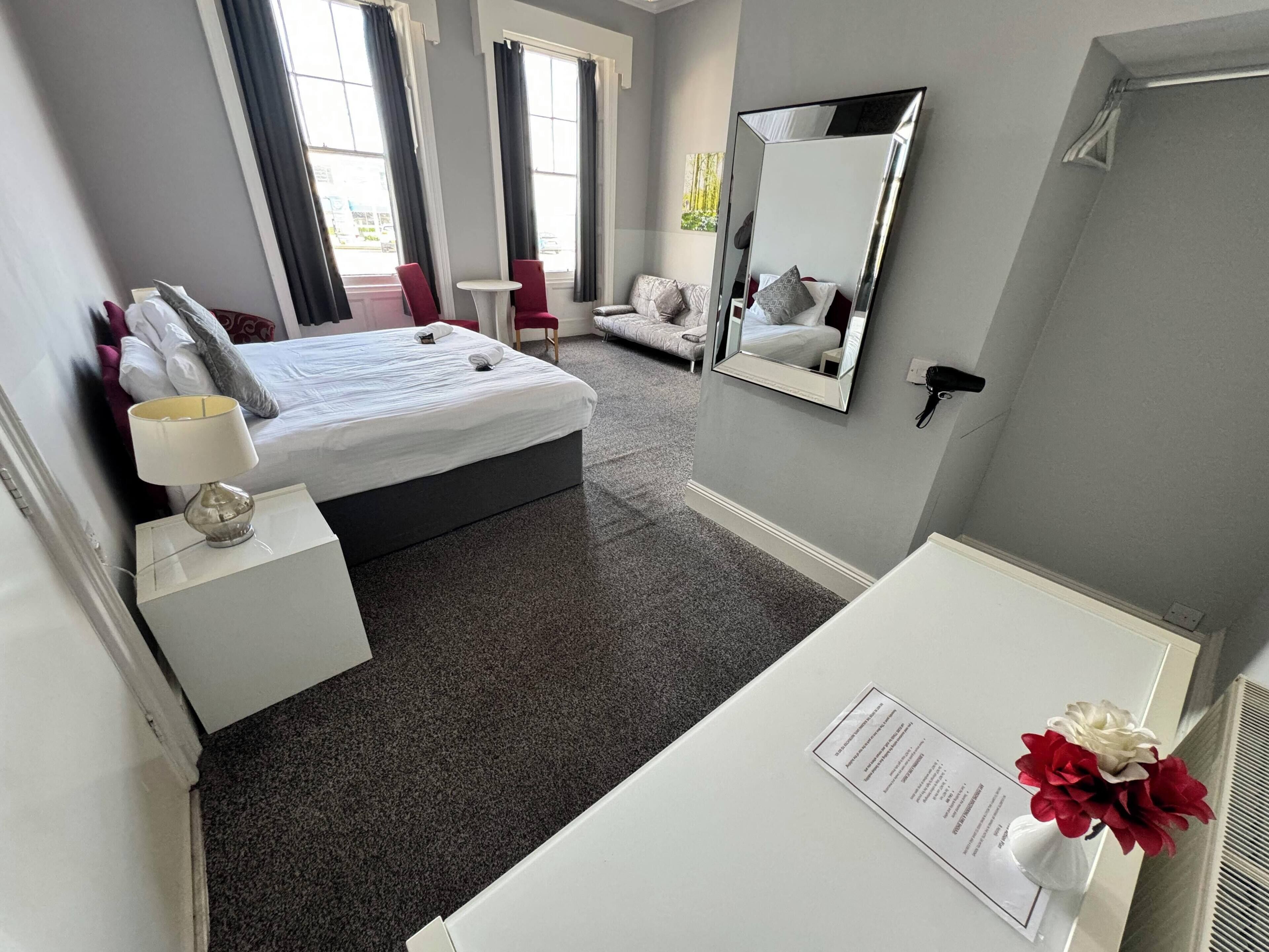 Una habitación de hotel con cama, mesita de noche, silla y un espejo grande.