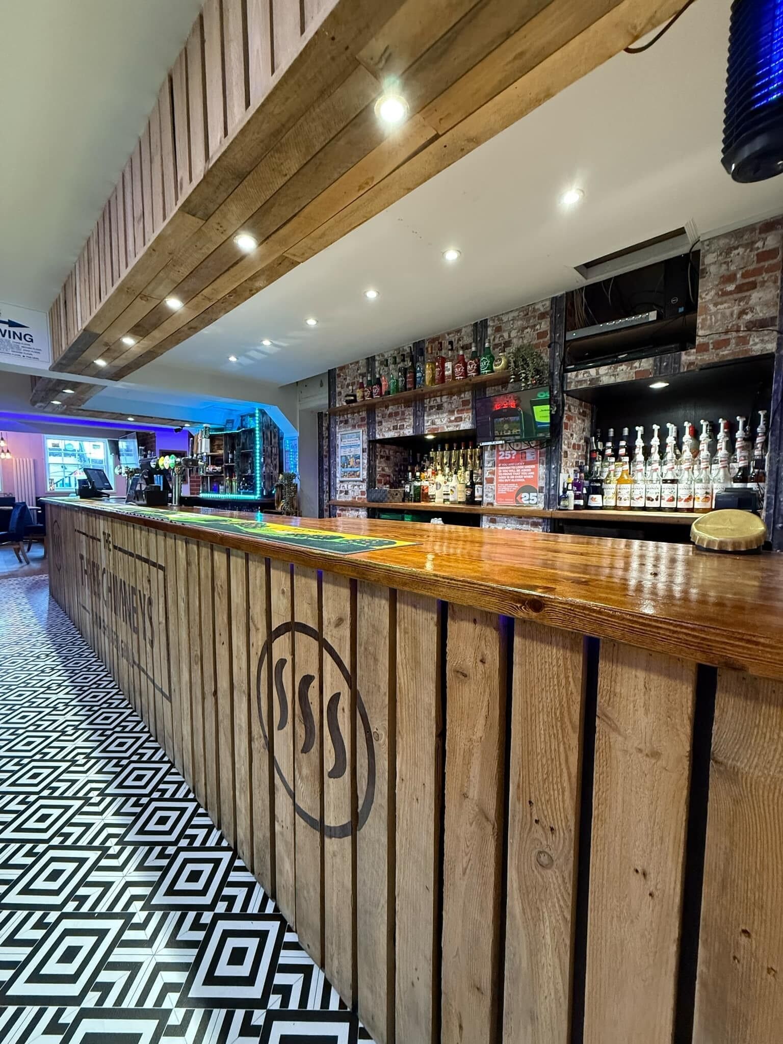 A bar area with a wooden counter, a variety of bottles, and a patterned floor.