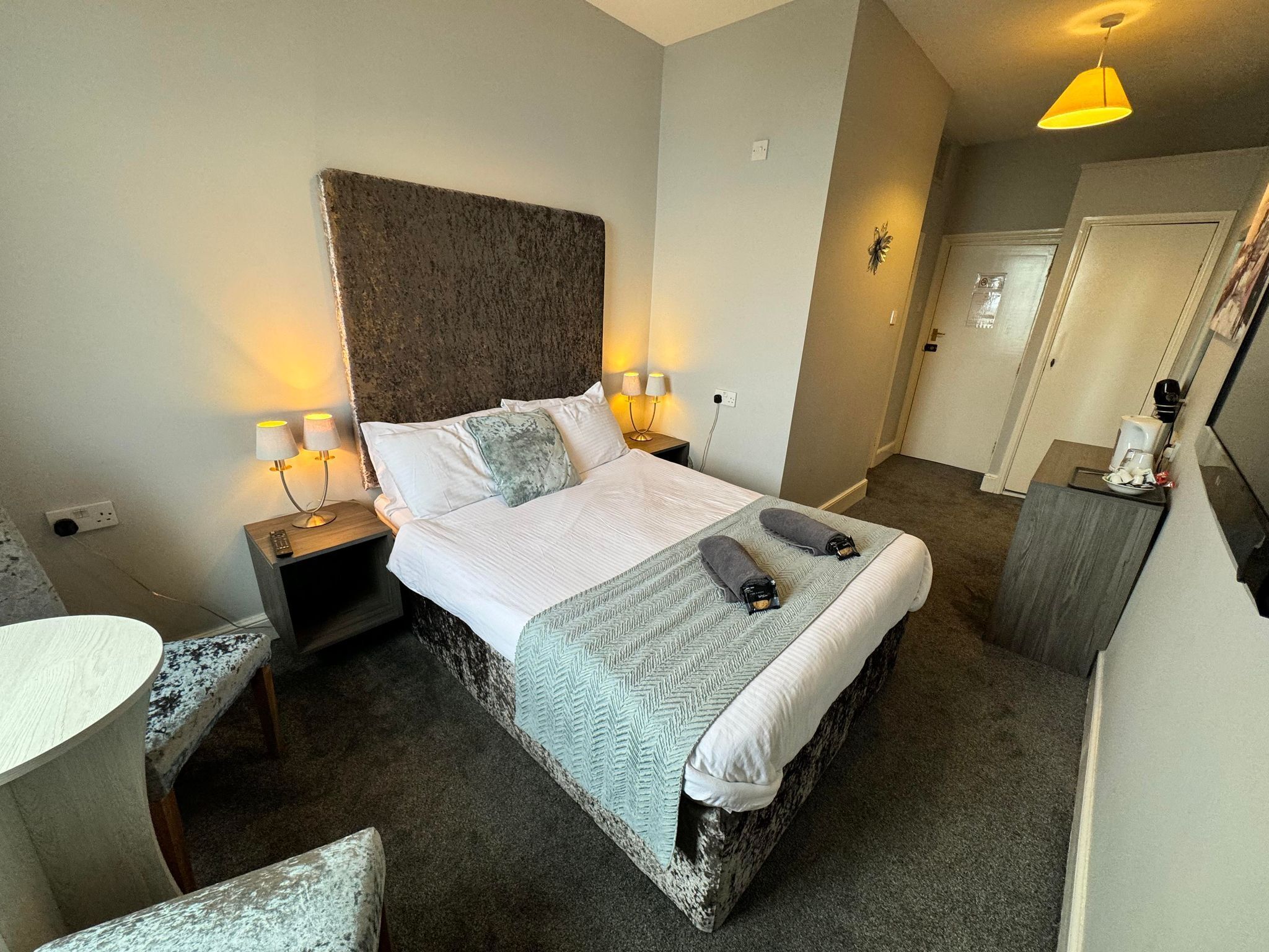 Una habitación de hotel con cama, lámparas de noche, escritorio y espejo.
