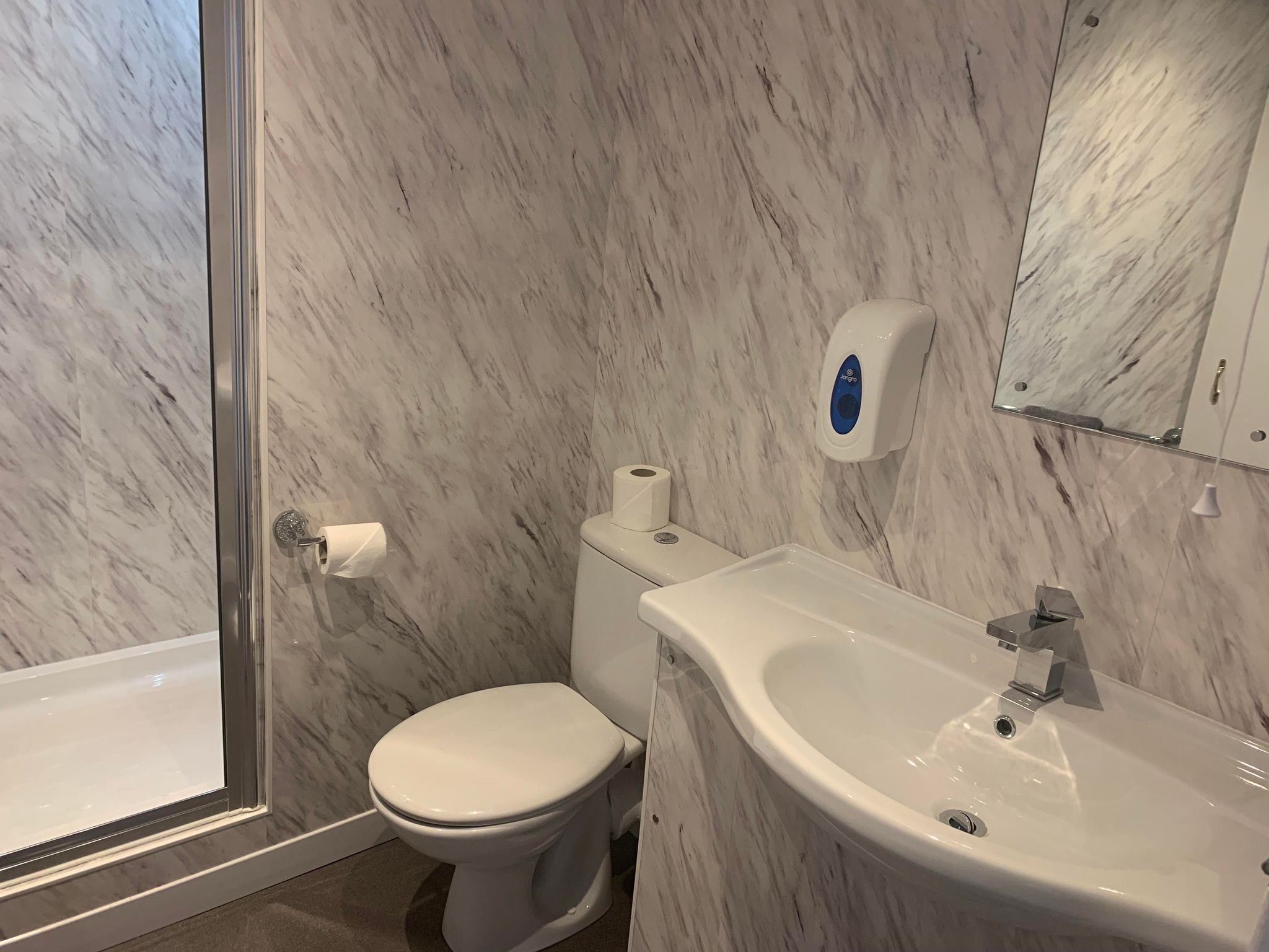 Ein Badezimmer mit Marmorwand, Toilette, Waschbecken und Duschbereich.