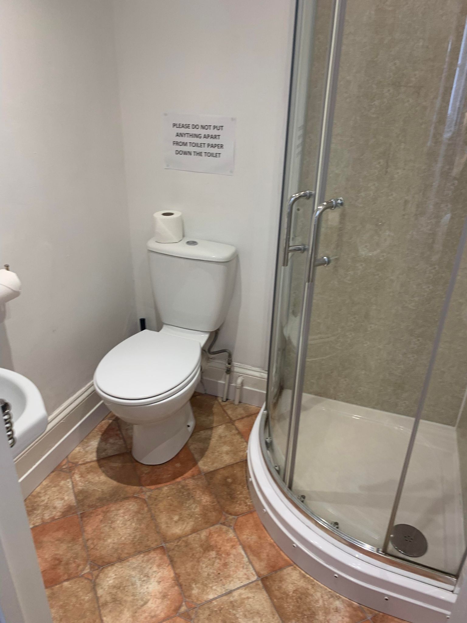 Casa de banho com sanita, cabine de duche em vidro e aviso a indicar para não colocar nada além de papel higiénico na sanita.