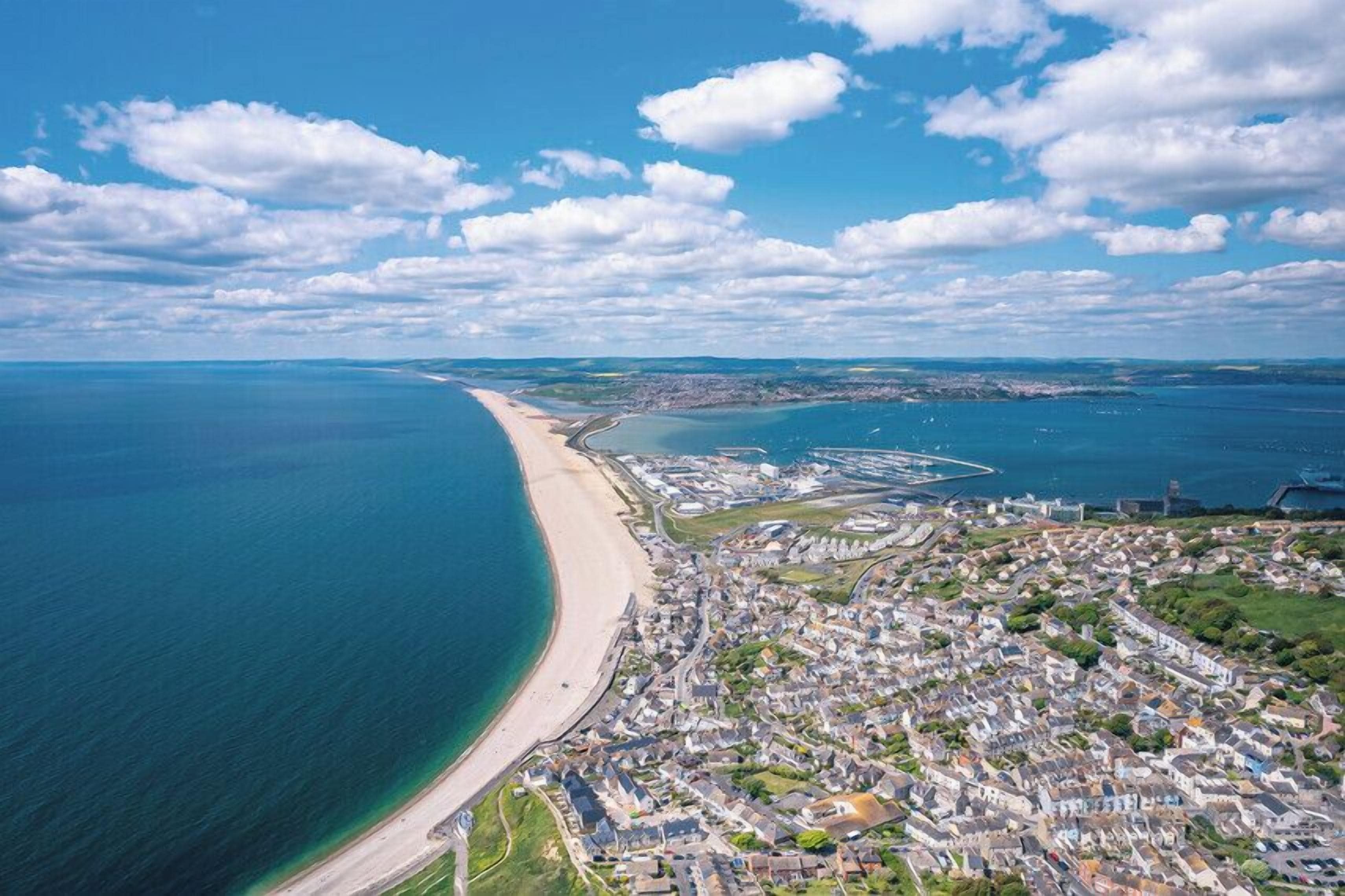 An aerial view of a coastal city with a beach, dense urban area, and a large body of water.