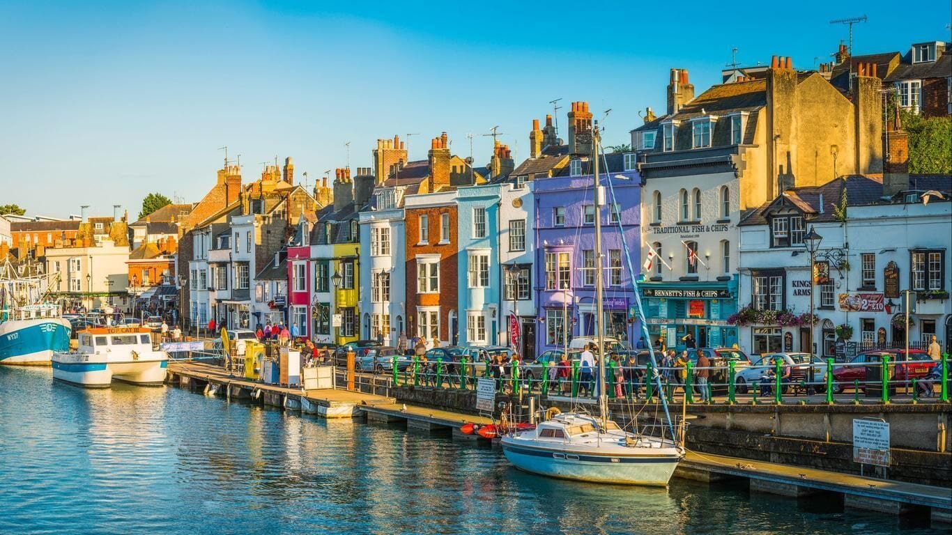 A waterfront with colorful buildings, a dock with boats, and a sign for 'Traditional Fish & Chips.'