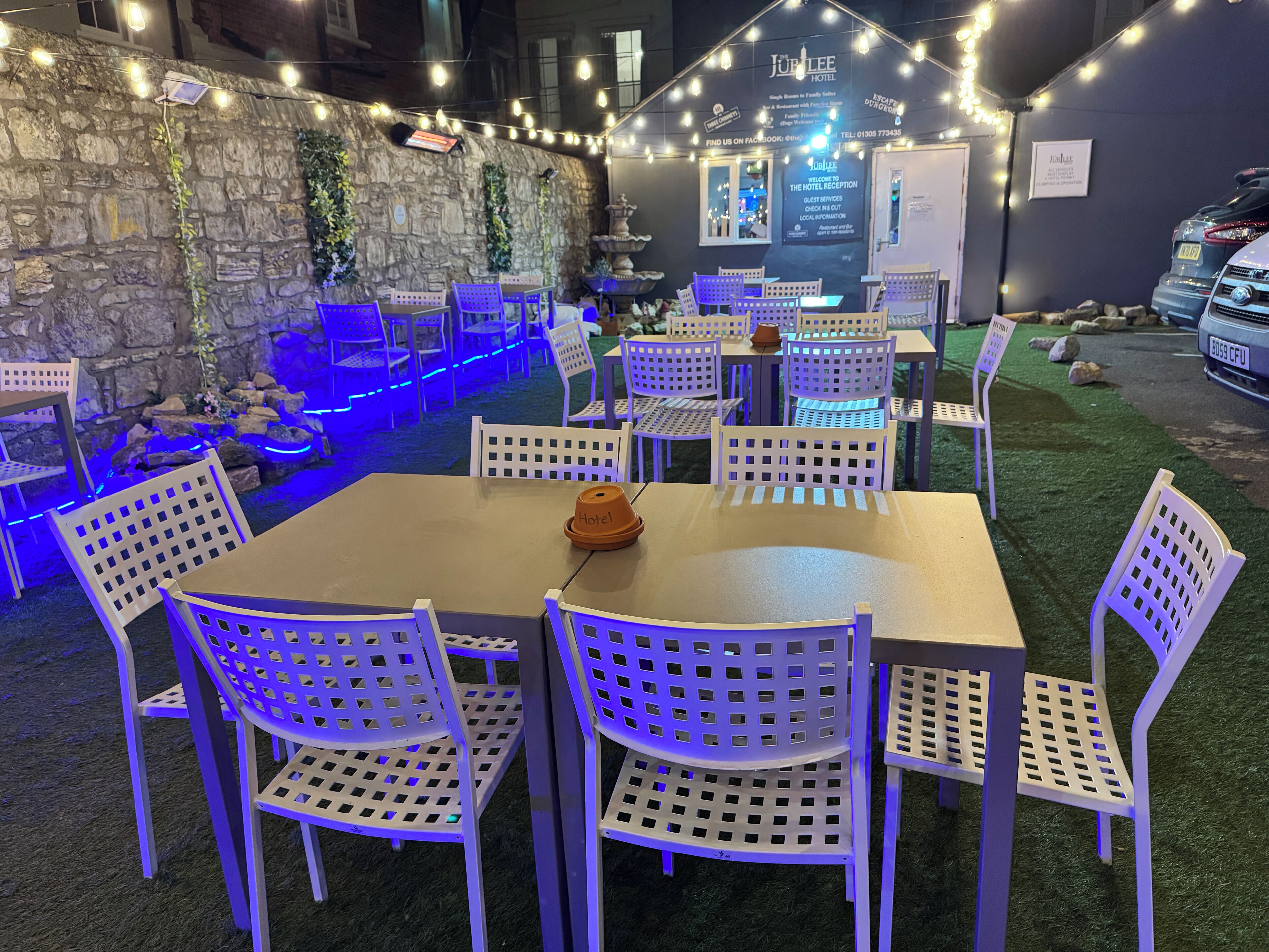 An outdoor seating area with tables and chairs, a stone wall, and string lights.