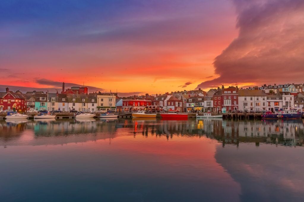 Uma cidade à beira-mar, com edifícios ao longo da costa e barcos atracados na água.